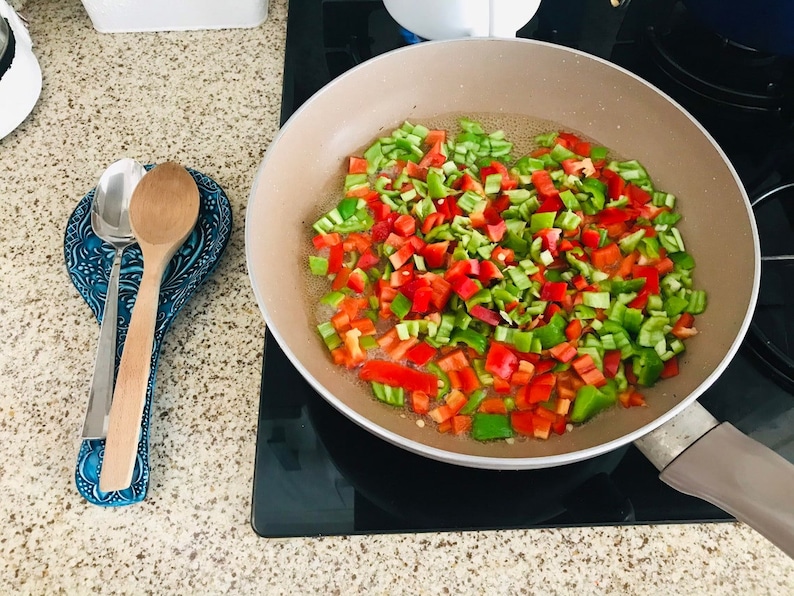 Pode incluir: Um close-up de uma panela com piment&otilde;es vermelhos e verdes picados cozinhando em &oacute;leo em um fog&atilde;o.
