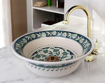 May include: A white ceramic sink with a green and white floral design. The sink has a gold-colored drain and is paired with a gold-colored faucet.