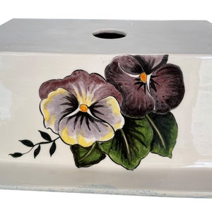 May include: White ceramic box with a hole in the top and a hand-painted design of purple and yellow pansies with green leaves.
