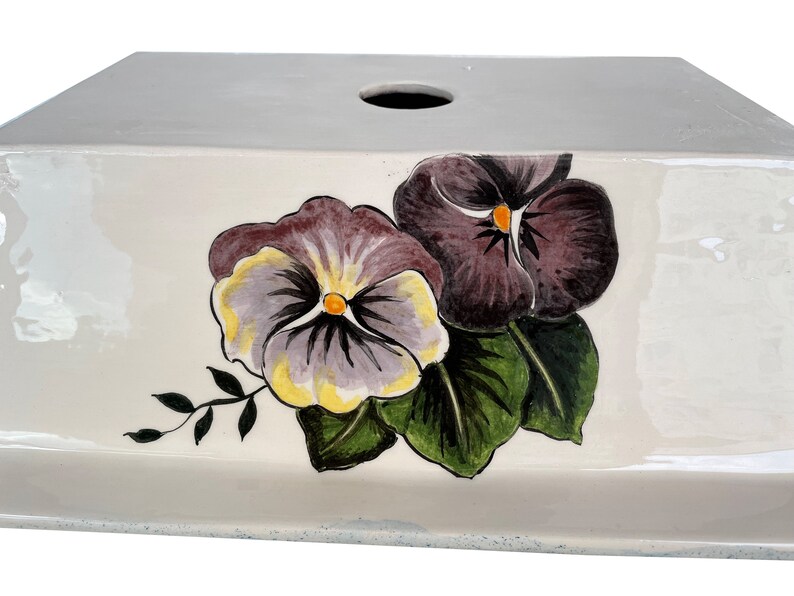 May include: White ceramic box with a hole in the top and a hand-painted design of purple and yellow pansies with green leaves.