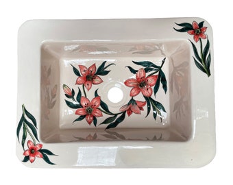 May include: A white ceramic bathroom sink with a floral design. The sink has a single drain hole and is decorated with pink flowers and green leaves.