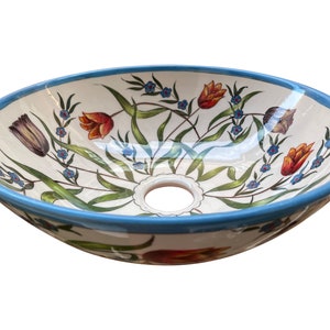 May include: A white ceramic oval sink with a blue rim and a floral design featuring red, orange, and blue flowers. The sink has a drain hole in the centre.