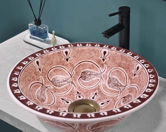 Puede incluir: Un lavabo de baño de cerámica con un diseño floral marrón y blanco. El lavabo es redondo y tiene un borde blanco. El lavabo está sobre una encimera blanca.