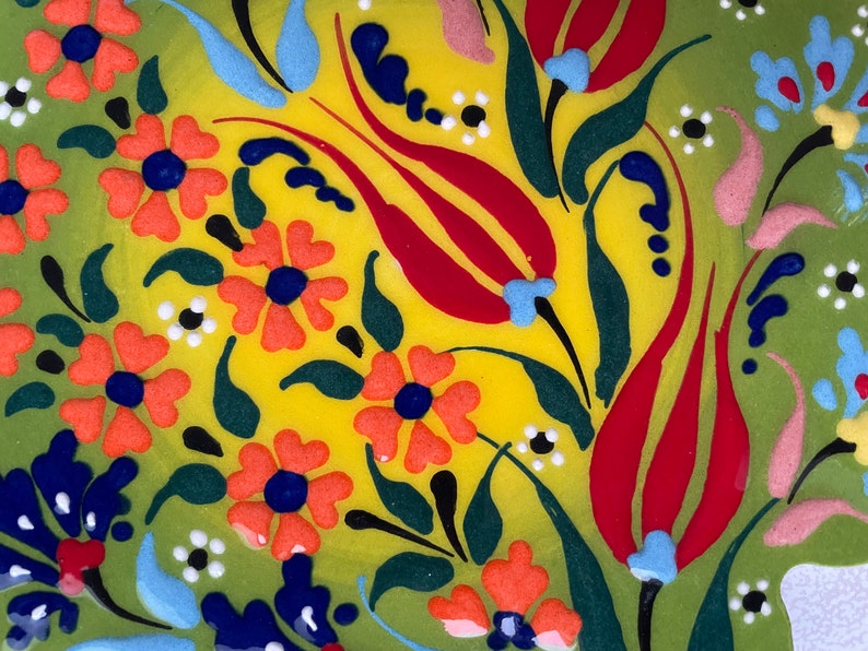 May include: A green and yellow ceramic plate with a floral design. The design features red, orange, blue, and white flowers and leaves.