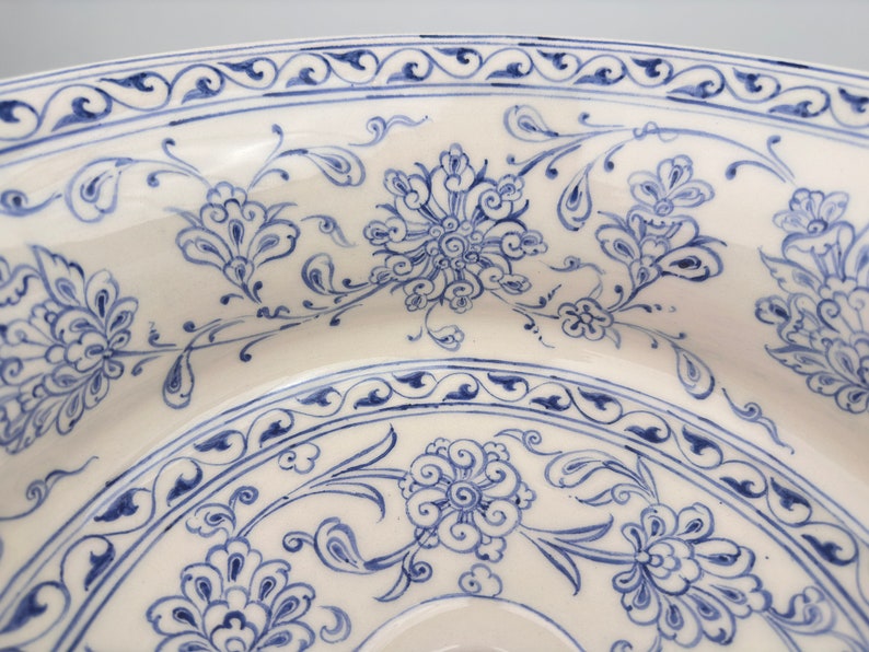 May include: A white ceramic plate with a blue and white floral design. The plate has a scalloped edge and a raised rim.