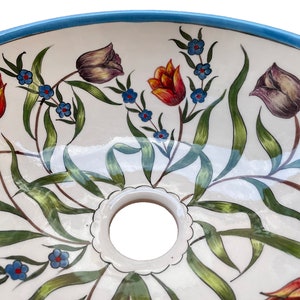 May include: A white ceramic sink with a blue rim and a floral design featuring red, orange, purple, and green tulips and blue flowers.