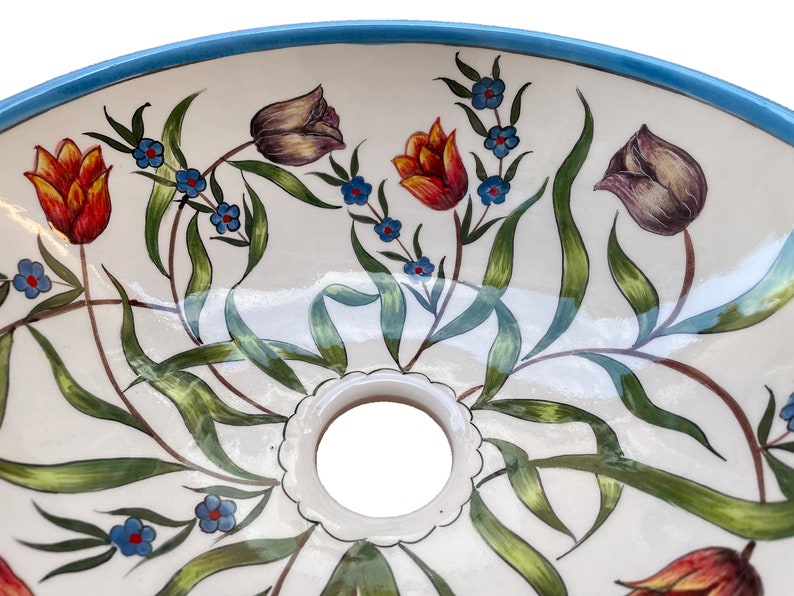 May include: A white ceramic sink with a blue rim and a floral design featuring red, orange, purple, and green tulips and blue flowers.