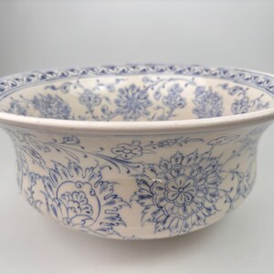 May include: A white ceramic bowl with a blue and white floral pattern. The bowl has a wide rim and a rounded bottom.