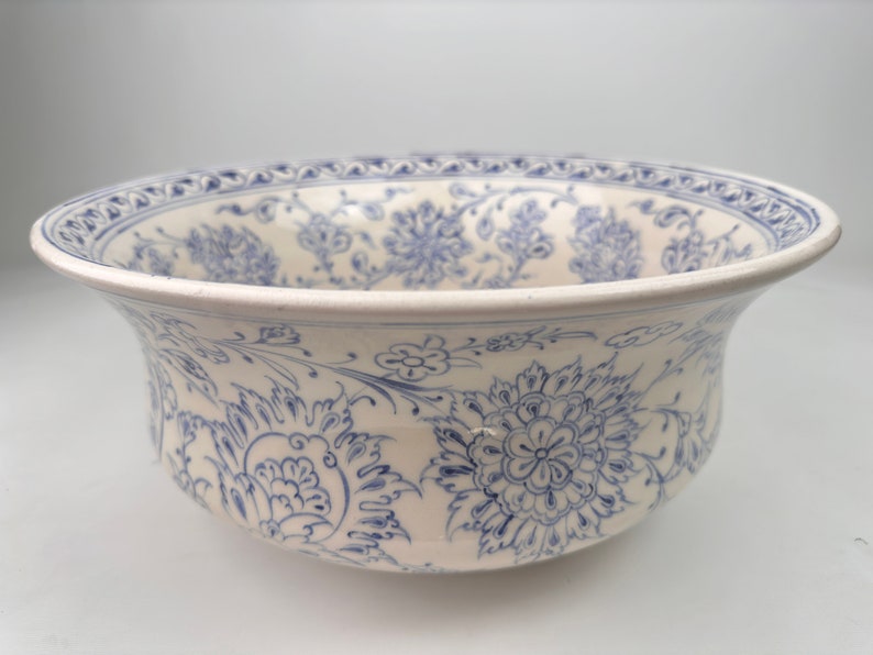 May include: A white ceramic bowl with a blue and white floral pattern. The bowl has a wide rim and a rounded bottom.