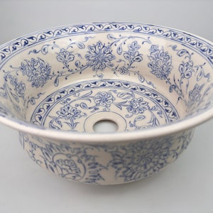 May include: A white ceramic sink with a blue and white floral pattern. The sink has a round shape and a drain hole in the center.