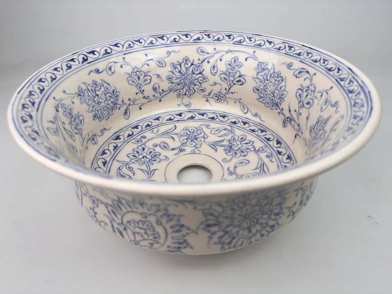May include: A white ceramic sink with a blue and white floral pattern. The sink has a round shape and a drain hole in the center.