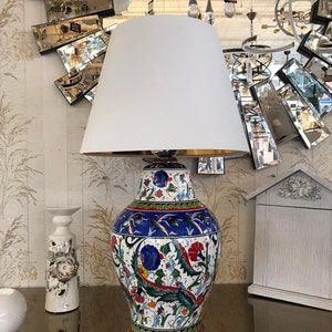 Peut inclure: Une lampe de table en c&eacute;ramique blanche avec un abat-jour blanc. Le pied de la lampe pr&eacute;sente un motif floral color&eacute; dans les tons bleu, vert, rouge et jaune.