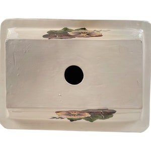 May include: White ceramic planter with a hole in the bottom and a floral design featuring purple and yellow pansies.
