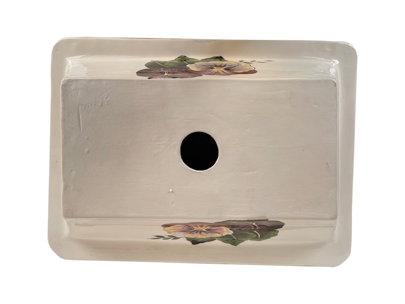 May include: White ceramic planter with a hole in the bottom and a floral design featuring purple and yellow pansies.