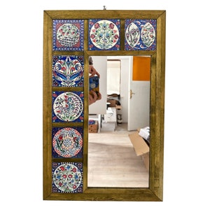 Puede incluir: Un espejo rectangular con marco de madera y un borde decorativo de ocho azulejos de cerámica coloridos con diseños florales. Los azulejos son en tonos de azul, rojo, blanco y verde.