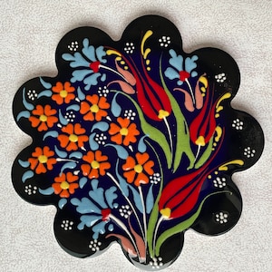 Pode incluir: Um azulejo de cerâmica com fundo azul e um desenho floral. O desenho apresenta flores e folhas vermelhas, laranja, amarelas e verdes.