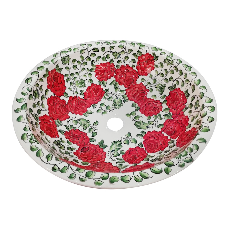 May include: White ceramic sink with a red and green floral design. The sink has a round shape and a single drain hole in the center.