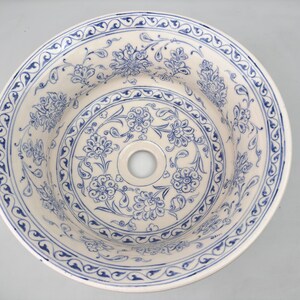 May include: A white ceramic sink with a blue and white floral pattern. The sink has a round shape and a single drain hole in the center.
