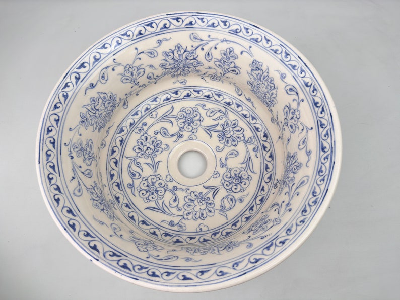 May include: A white ceramic sink with a blue and white floral pattern. The sink has a round shape and a single drain hole in the center.