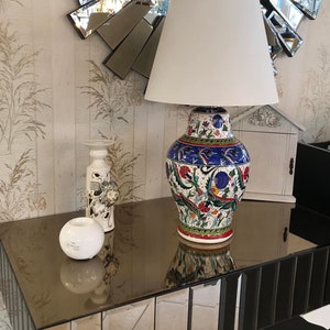 Peut inclure: Une lampe blanche avec un abat-jour blanc est pos&eacute;e sur une table en miroir avec un vase en c&eacute;ramique d&eacute;coratif aux motifs floraux color&eacute;s. Le vase est bleu, rouge, vert et blanc.