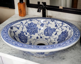 May include: A white ceramic sink with a blue and white floral design. The sink is oval shaped and has a drain in the center.