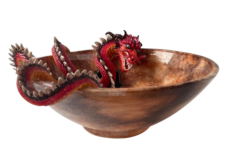 May include: A decorative bowl featuring a red and black dragon design. The dragon is emerging from the bowl, which has a brown, textured finish. The dragon has sharp teeth and a spiked tail.
