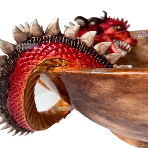 May include: A decorative bowl with a dragon design. The dragon has red scales, brown spines, and a detailed head. The bowl has a brown, textured finish, creating a fantasy-themed decorative piece.