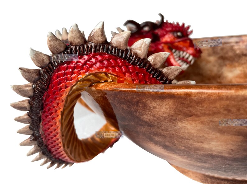 May include: A decorative bowl with a dragon design. The dragon has red scales, brown spines, and a detailed head. The bowl has a brown, textured finish, creating a fantasy-themed decorative piece.