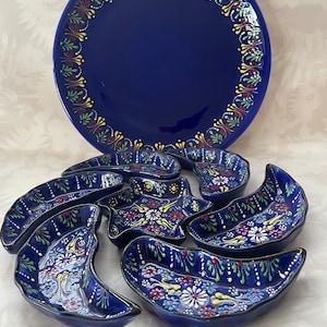 Könnte beinhalten: Ein Set aus blauen und weißen Keramik-Servierplatten mit Blumenmustern. Das Set enthält eine große runde Platte und sechs kleinere, sichelförmige Schalen.