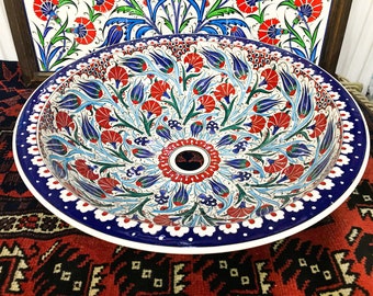 Könnte beinhalten: Ein weißes Keramikwaschbecken mit einem blauen und weißen Rand. Das Waschbecken ist mit einem traditionellen türkischen Blumenmuster in Rot-, Blau-, Grün- und Weißtönen verziert.