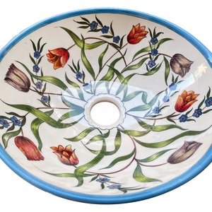 May include: A white ceramic sink with a blue rim and a floral design featuring tulips, leaves, and small blue flowers.