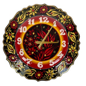May include: A black, red, and yellow ceramic clock with a floral design. The clock face has white numbers and gold hands.