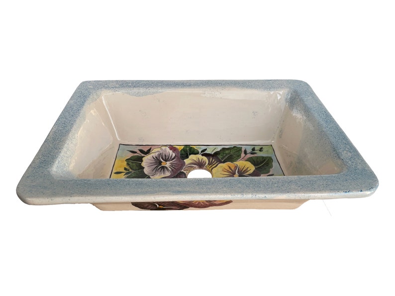 May include: A white ceramic sink with a blue rim and a painted floral design featuring purple and yellow pansies.