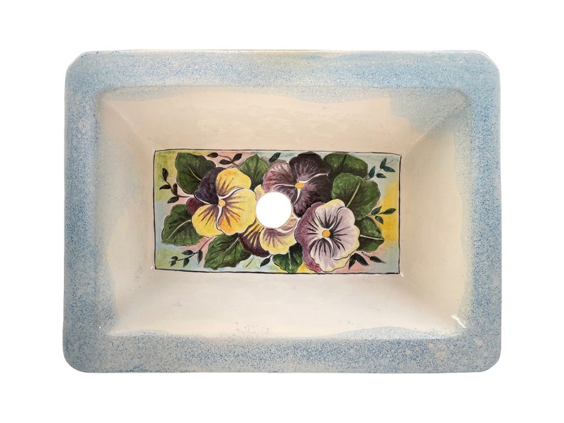 May include: A white ceramic bathroom sink with a blue rim and a floral design featuring yellow and purple pansies. The sink has a single drain hole.