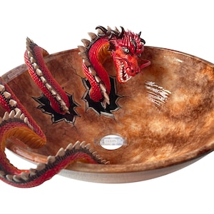 May include: An oval bathroom sink with a brown and tan mottled finish. A red dragon with white teeth and a long tail appears to be breaking through the sink's surface. The dragon's head and tail are visible, adding a fantasy theme.