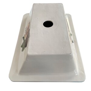 May include: White ceramic sink with a floral design and a drain hole in the center. The sink is rectangular and has a raised rim.