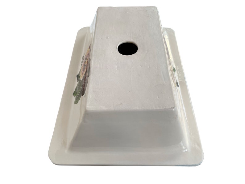May include: White ceramic sink with a floral design and a drain hole in the center. The sink is rectangular and has a raised rim.
