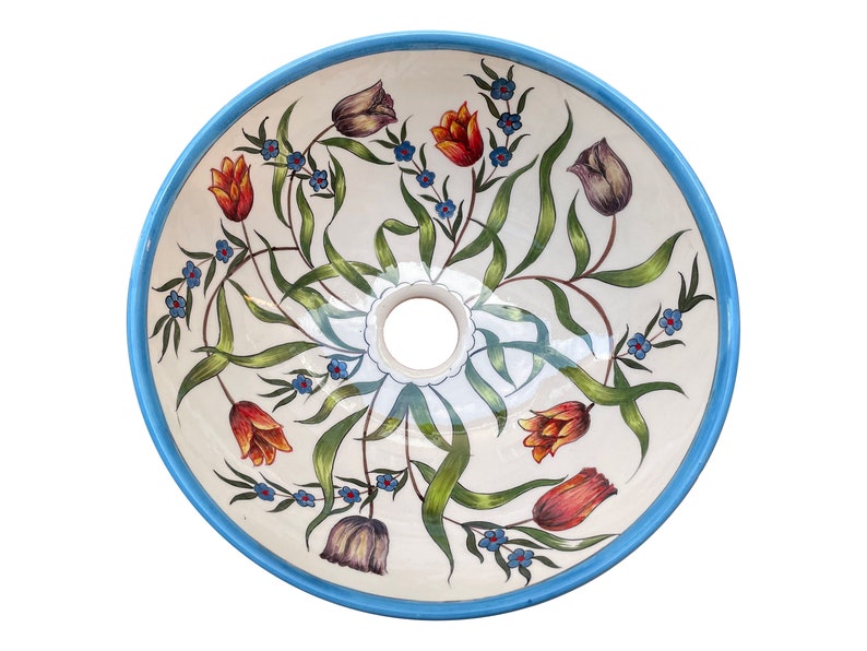 May include: A white ceramic sink with a blue rim and a floral design featuring tulips and small blue flowers. The sink is round and has a drain hole in the centre.