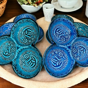 May include: A collection of blue ceramic serving dishes with a unique three-section design. Each dish features intricate floral and scroll patterns in white against a vibrant blue background. The dishes are arranged on a beige woven placemat, showcasing their decorative appeal.