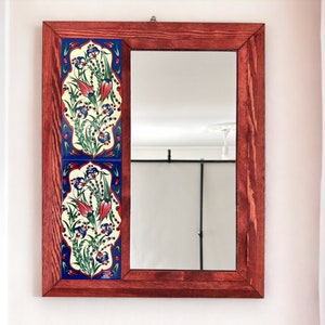 Puede incluir: Un espejo rectangular con un marco de madera oscura y un diseño de azulejos decorativos en el lado izquierdo. El diseño de los azulejos presenta un patrón floral en tonos de azul, rojo y blanco.