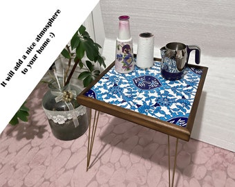 May include: A small wooden table with a blue and white patterned tile top. The table has gold metal legs and is decorated with a blue and white patterned vase and a silver pitcher.