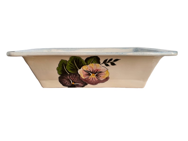 May include: A white ceramic baking dish with a floral design featuring purple and pink pansies with green leaves. The dish has a slightly raised rim.