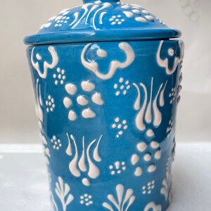 Op de afbeelding: Een blauwe keramische pot met een deksel, met een wit bloemenpatroon. De pot heeft een ronde vorm en een gladde, glanzende afwerking.