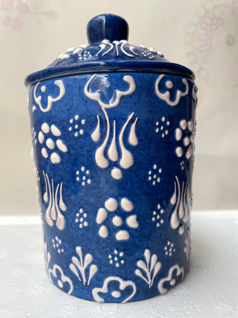Op de afbeelding: Een blauwe keramische pot met een wit deksel en witte bloemmotieven. De pot heeft een traditioneel Turks ontwerp.
