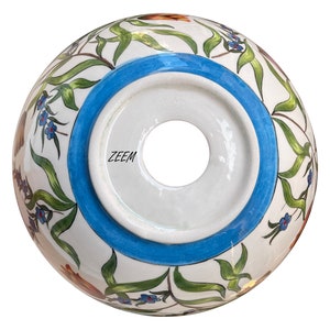 May include: The underside of a white ceramic bowl with a blue rim and floral design. The bowl has a hole in the centre and the word "ZEEM" is printed on the bottom.