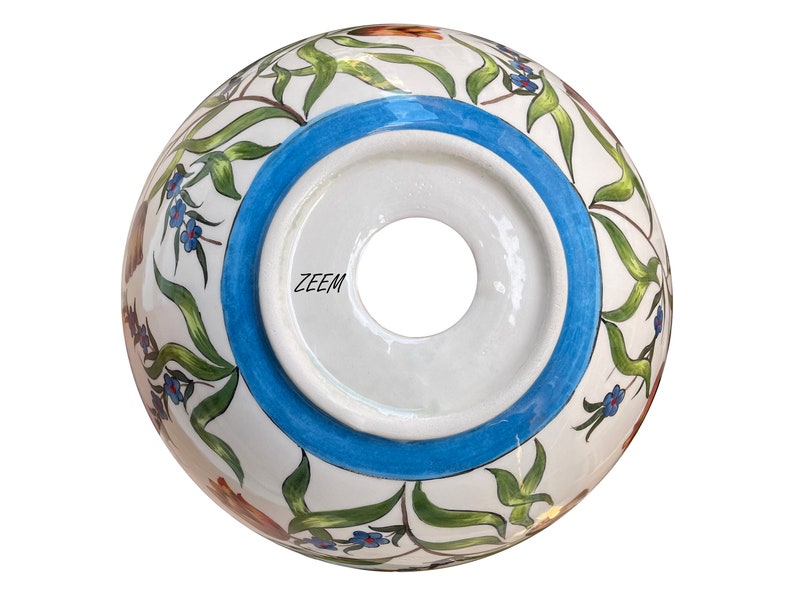 May include: The underside of a white ceramic bowl with a blue rim and floral design. The bowl has a hole in the centre and the word "ZEEM" is printed on the bottom.