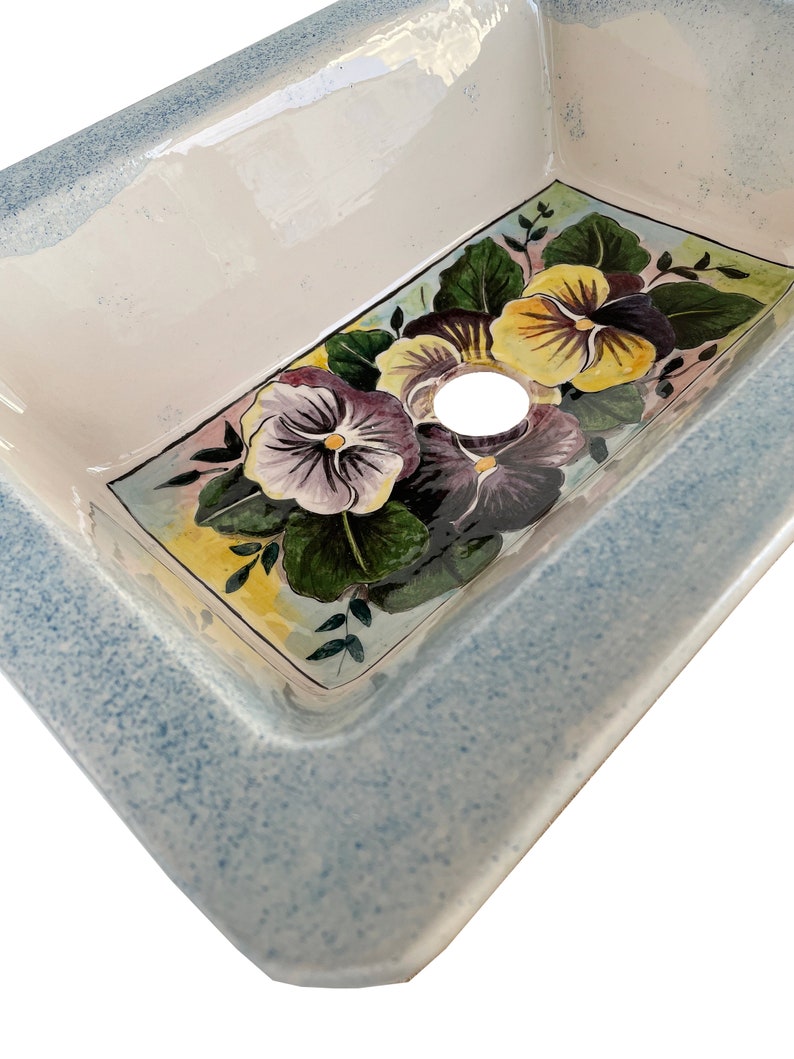 May include: A white ceramic sink with a blue rim and a floral design featuring purple, yellow, and green pansies.