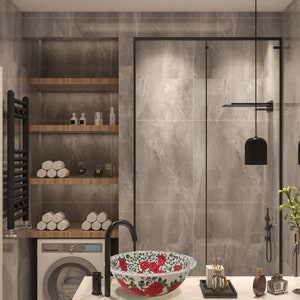 May include: A modern bathroom with a white porcelain sink with a floral design. The sink is on a white countertop with a black faucet. There is a black towel rack, a white washing machine, and a glass shower door in the background.