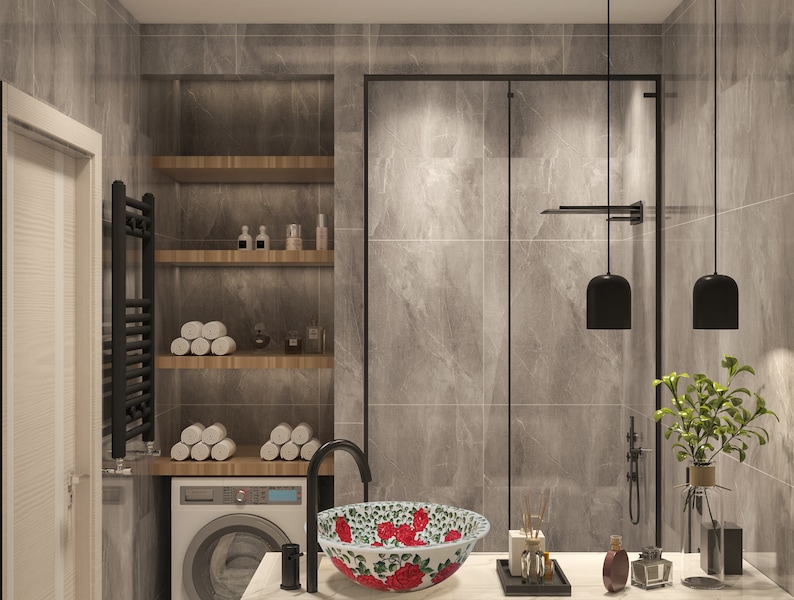 May include: A modern bathroom with a white porcelain sink with a floral design. The sink is on a white countertop with a black faucet. There is a black towel rack, a white washing machine, and a glass shower door in the background.