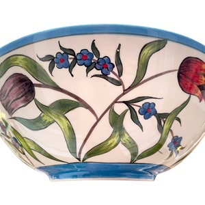 May include: A white ceramic bowl with a blue rim and floral design. The bowl features hand-painted tulips, leaves, and small blue flowers.